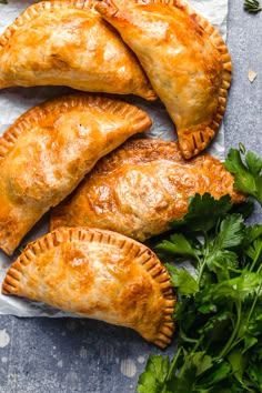 four empanada pastries on a piece of parchment paper with parsley next to them