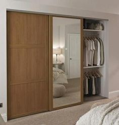 a bedroom with a bed, mirror and closet doors that are open to reveal clothes on hangers