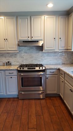 a kitchen with white cabinets and stainless steel stove top oven, wood flooring and hardwood floors