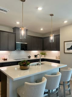 a kitchen with an island and bar stools next to the counter top, lights above it