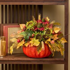 a vase filled with flowers and leaves on top of a wooden shelf