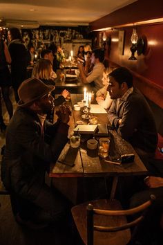 several people sitting at a table in a restaurant with candles on the tables and one person holding a cell phone up to his ear