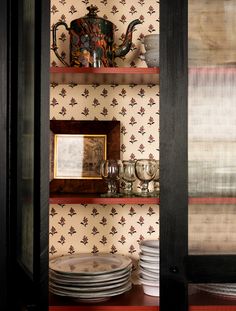 a shelf with plates and cups on it in front of a wallpapered wall