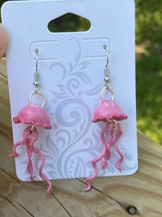 a pair of pink jellyfish earrings sitting on top of a piece of wood next to a card