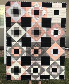 a woman standing in front of a black and white quilt on the grass with her hands behind her back