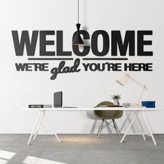 a desk with a computer on it in front of a wall that says welcome, we're glad you're here