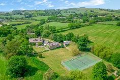 an aerial view of a tennis court in the middle of a green field with trees