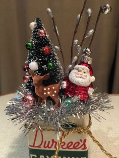 a small christmas tree in a tin can with ornaments on it and a santa clause ornament hanging from the top