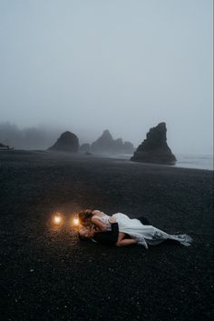 a woman laying on the ground next to two candles in front of some rocks and water