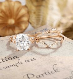 an engagement ring and wedding band on top of a piece of paper with other items in the background