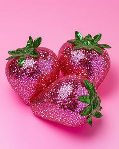 three shiny strawberries with green leaves on pink background, one is purple and the other is red