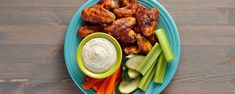 a blue plate topped with chicken wings, celery and carrots