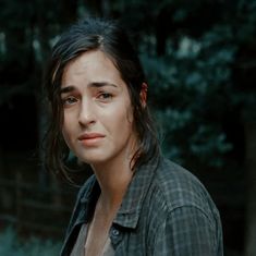 a woman standing in front of trees with her eyes closed and looking at the camera