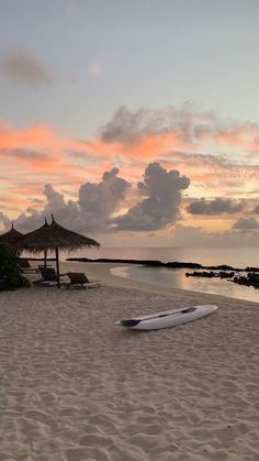 a white surfboard sitting on top of a sandy beach under a pink and blue sky