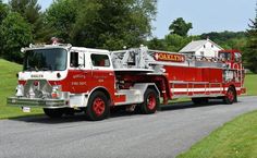 a red and white fire truck driving down a street next to a lush green field