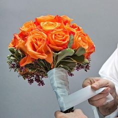 a man holding a bouquet of orange roses in it's left hand while another person holds a piece of paper