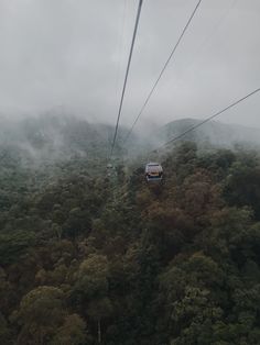 the cable car is going over the trees in the foggy sky above the mountains