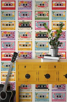 a colorful wallpaper with cassette tape and a plant on top of a yellow dresser