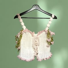 a white top with pink and green flowers hanging from a hanger on a green wall