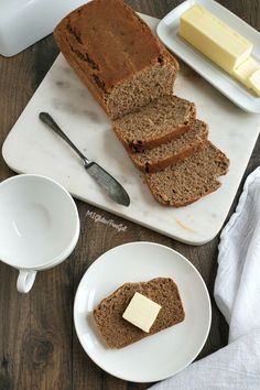 sliced loaf of bread on a cutting board with butter and two white plates next to it