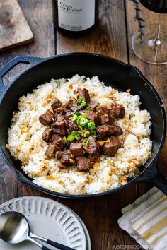 a pan filled with rice and meat on top of a wooden table next to a bottle of wine