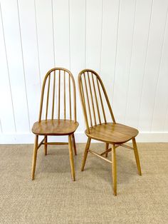 two wooden chairs sitting next to each other on top of a carpeted floor in front of a white wall