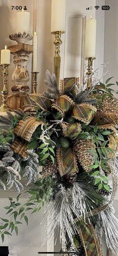 a christmas wreath with pine cones and evergreens in front of a fireplace mantel