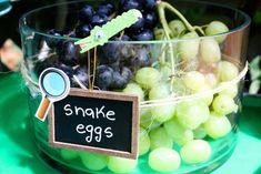 a glass bowl filled with green and black grapes next to a sign that says snake eggs