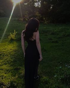 a woman in a black dress is standing in the grass with her back to the camera