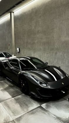 two black sports cars parked next to each other in a parking garage with concrete walls