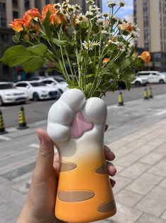 a hand holding a vase with flowers in it on the sidewalk next to a city street