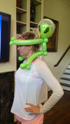 a woman standing in front of a tv wearing an alien balloon head