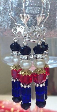 two pairs of earrings with pearls and beads on top of a glass stand in front of a cake