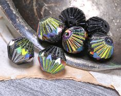 some black and silver beads are on a table next to a spoon with something in it