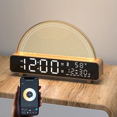 a person holding a cell phone in front of an alarm clock on a wooden table