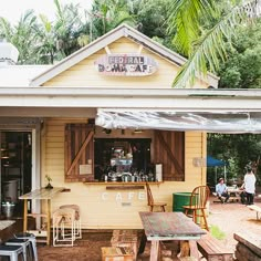 an outdoor cafe with wooden tables and chairs under a tarp over the front door