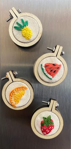 three embroidered fruit coasters sitting on top of a metal surface, with pineapple and watermelon in the center