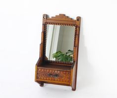 a wooden vanity with mirror and plant on it's stand against a white wall