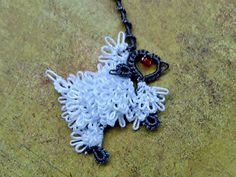 a white sheep is hanging from a black chain on a stone surface with a red bead in it's ear