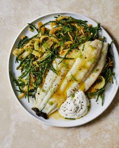 a white plate topped with fish covered in sauce and green vegetables on top of a table