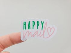 a hand holding a happy mail sticker in front of a white background with pink and green lettering