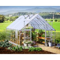 a small greenhouse in the middle of a field with lots of plants and flowers around it