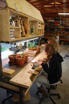 a woman sitting at a wooden table working on some woodworking projects in a workshop