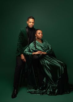 a man and woman sitting next to each other on a green background wearing black clothing