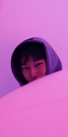 a young child wearing a hoodie peeking out from behind a pink wall with his eyes closed