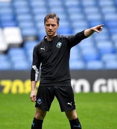 a man standing on top of a soccer field holding a ball in his hand and pointing to the side