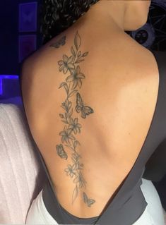 the back of a woman's shoulder with flowers and butterflies tattooed on her lower back