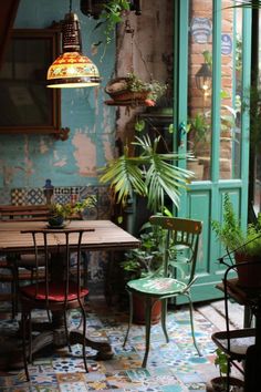 an outdoor dining area with potted plants on the table and hanging lights above it