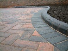 a brick walkway in the middle of a garden area with grass and dirt around it