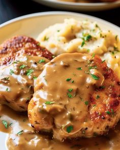 a white plate topped with meat and gravy covered in gravy next to mashed potatoes